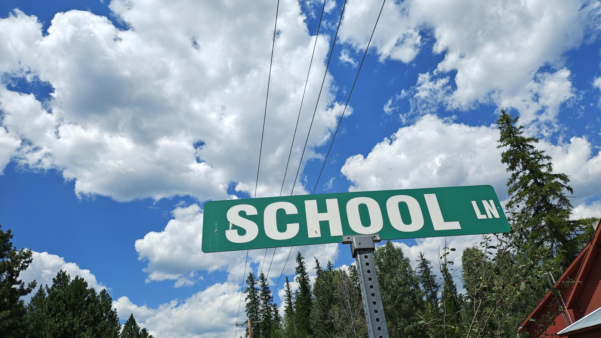 Green school lane sign under a blue sky with clouds.