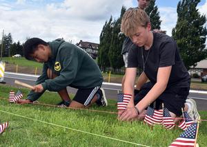 Two teens placing small American flags in grassy area.