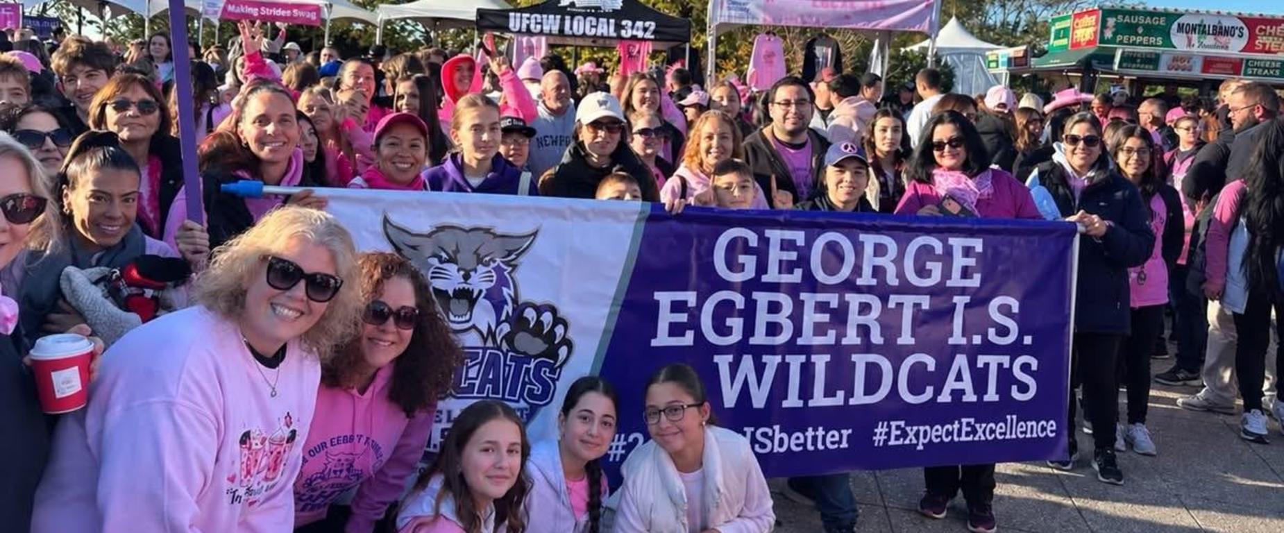 Large crowd of people in pink shirts holding banners at an event.
