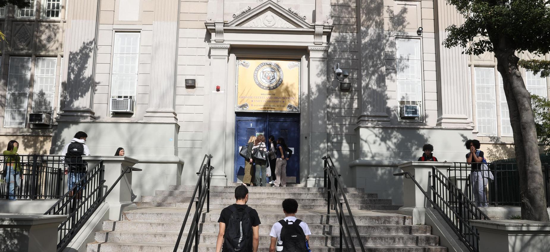 Students walking up steps toward a school entrance with a banner above the door.