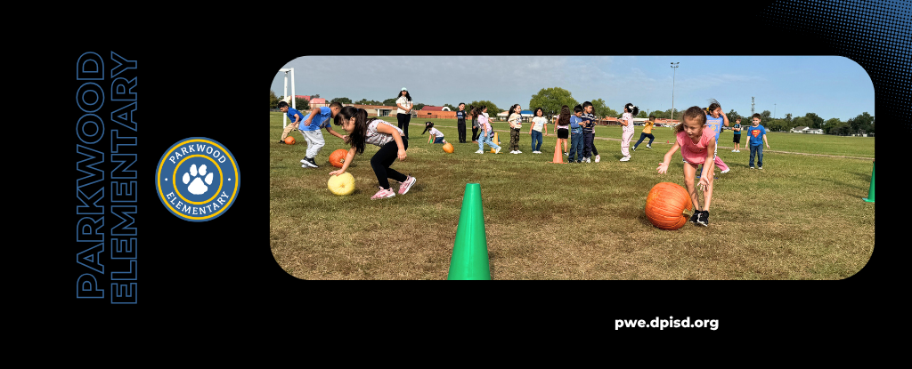 Children participating in an outdoor activity, rolling large pumpkins on grassy field.
