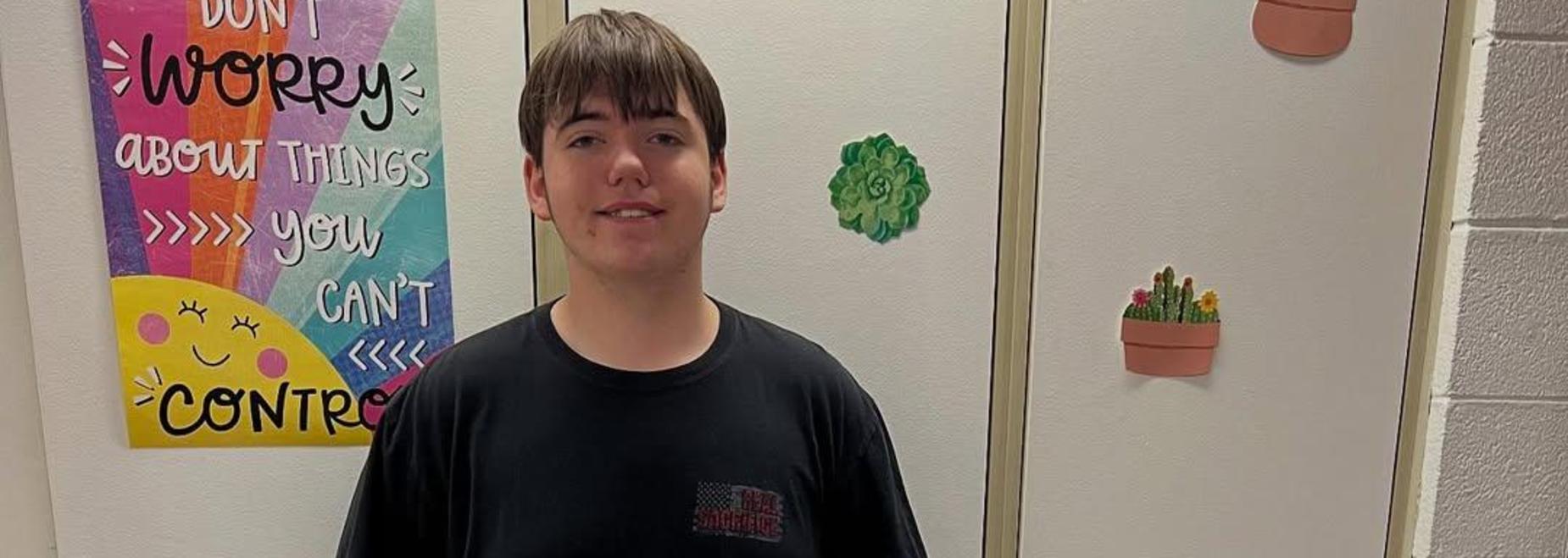 A boy stands confidently in a black shirt in front of decorated cabinets.