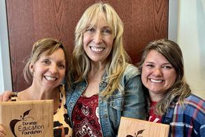 Three smiling adults hold wooden award plaques
