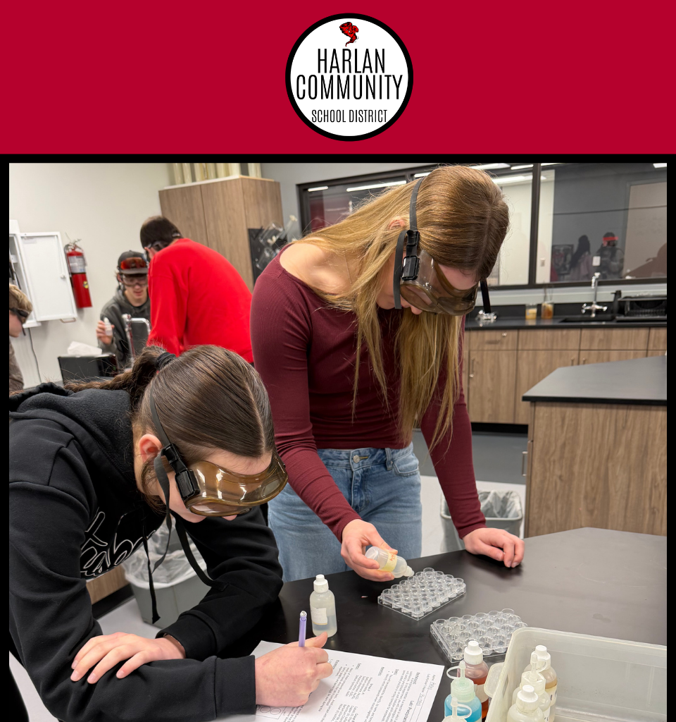 Two students in safety goggles conduct an experiment in a lab setting.