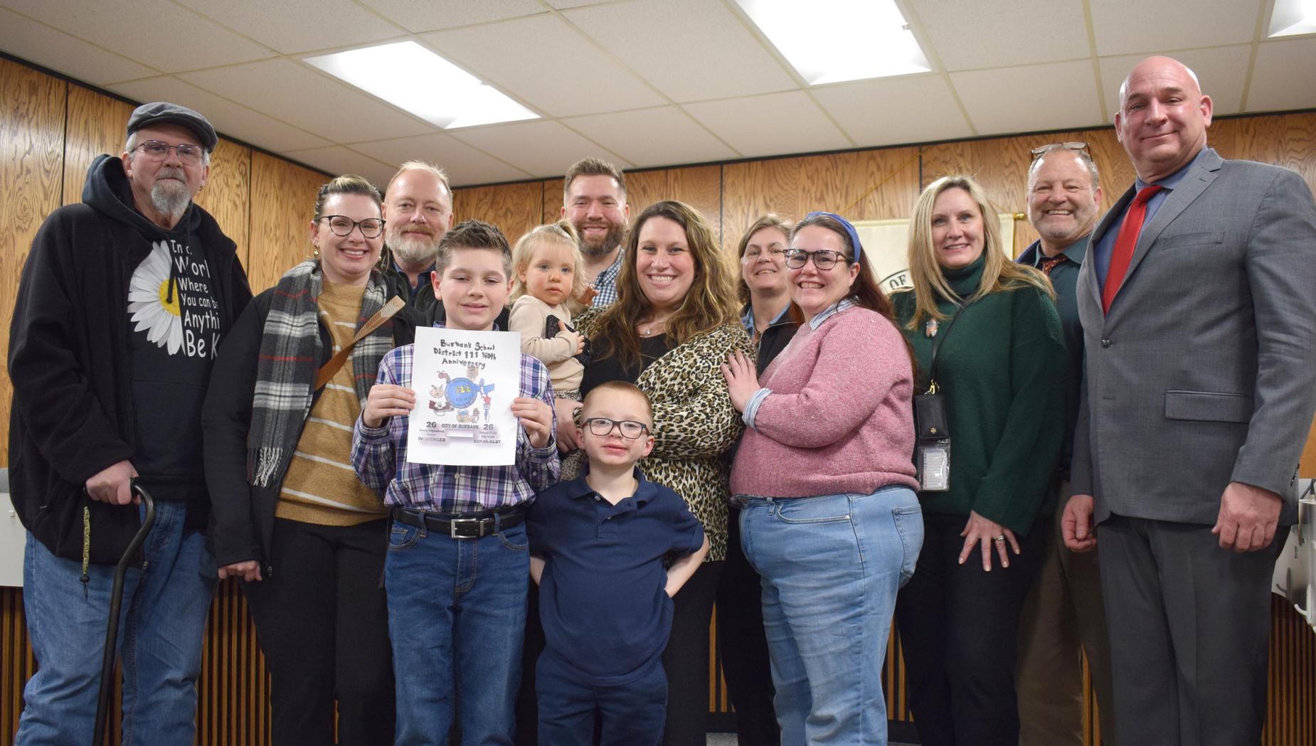 A group of people posing together, with children holding a certificate in front.