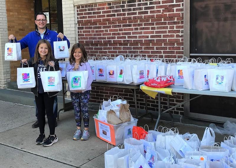 McKinley 4th grader Julia Kopec (left) and her 2nd grade sister Sophia join principal Marc Biunno in displaying student-designed Halloween trick or treat bags for U.S. troops to thank them for their service.