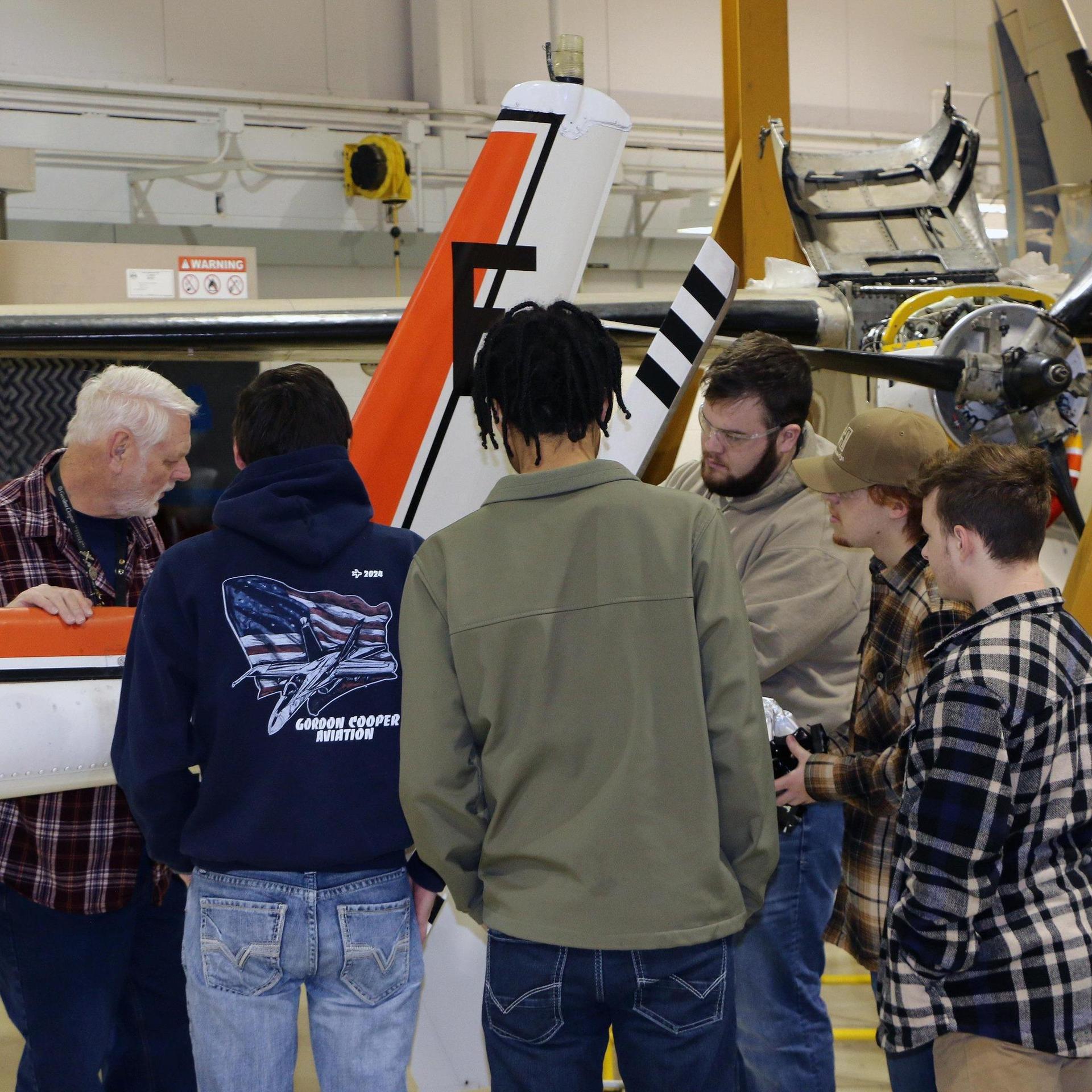 Instructor inspecting the tail of a helicopter with a group of students.