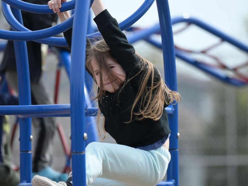 Child hanging from a playground structure with hair flowing in the wind.