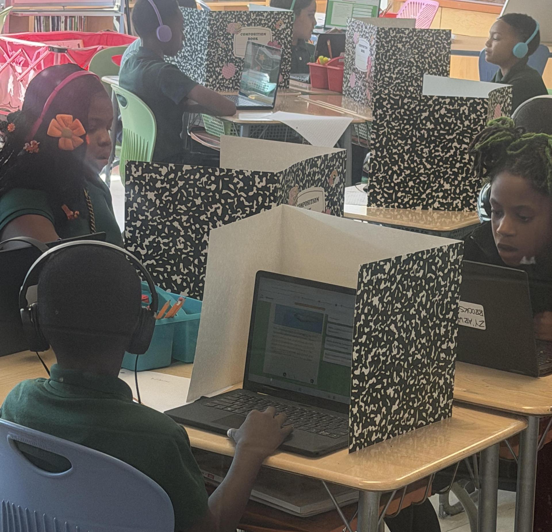 Students in a classroom using laptops behind partition screens.