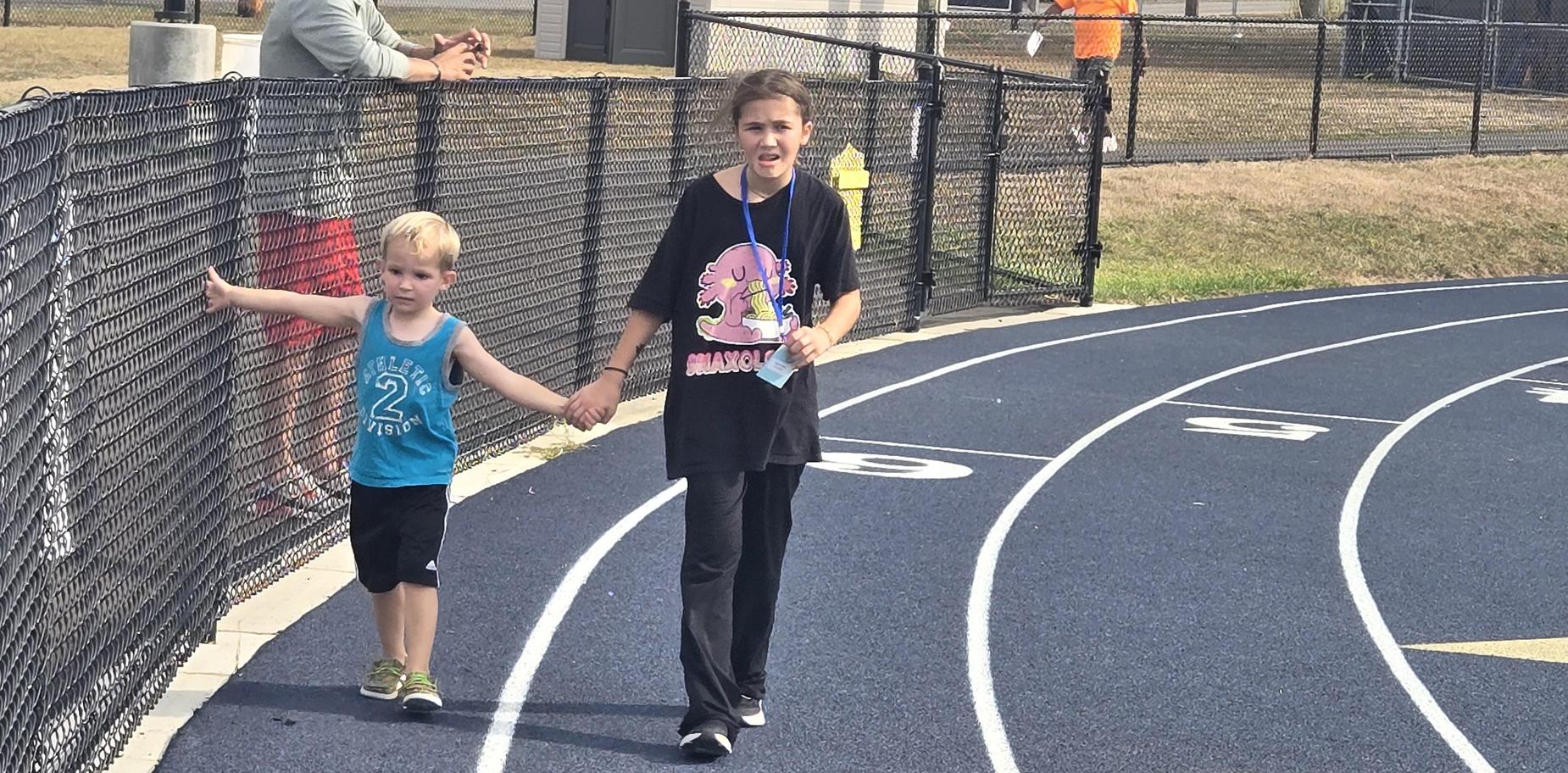 Child holding hands with an adult on a running track.
