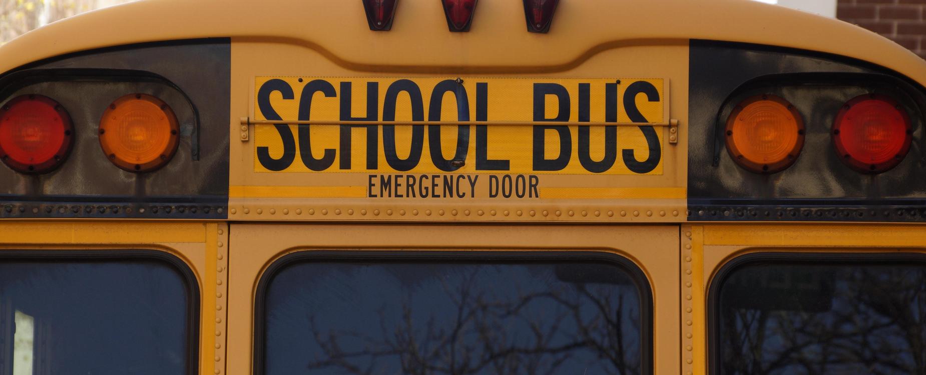 Back view of a yellow school bus with an emergency door sign.