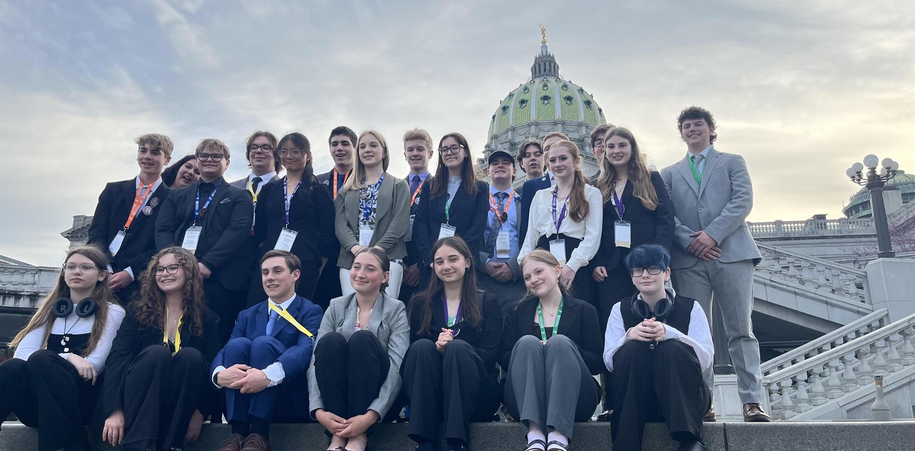 Large group of students in formal attire posing on steps of a government building.