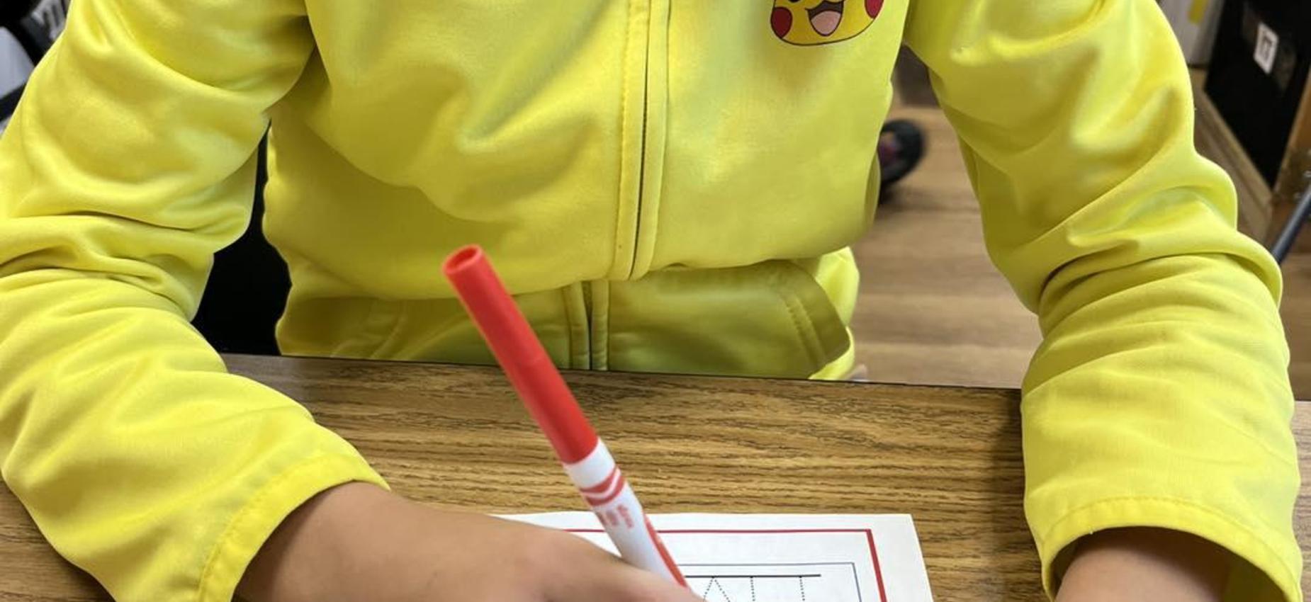 Child in a yellow jacket drawing with a red marker.