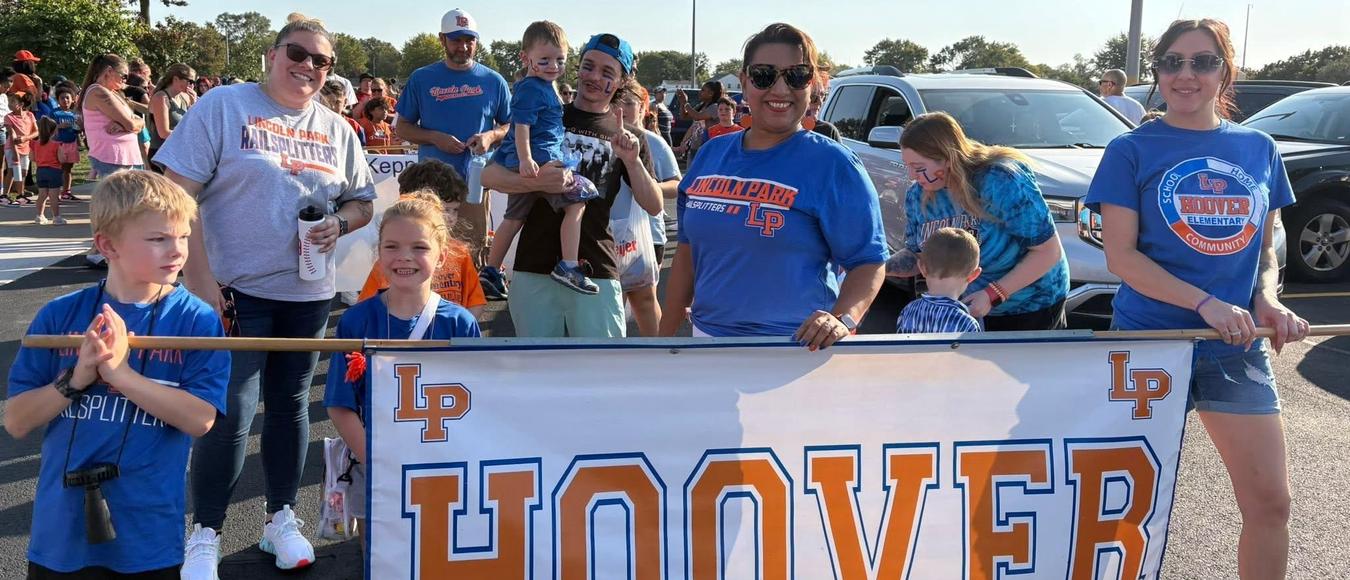 Hoover staff and students smile while holding a large white and orange "HOOVER" school banner.