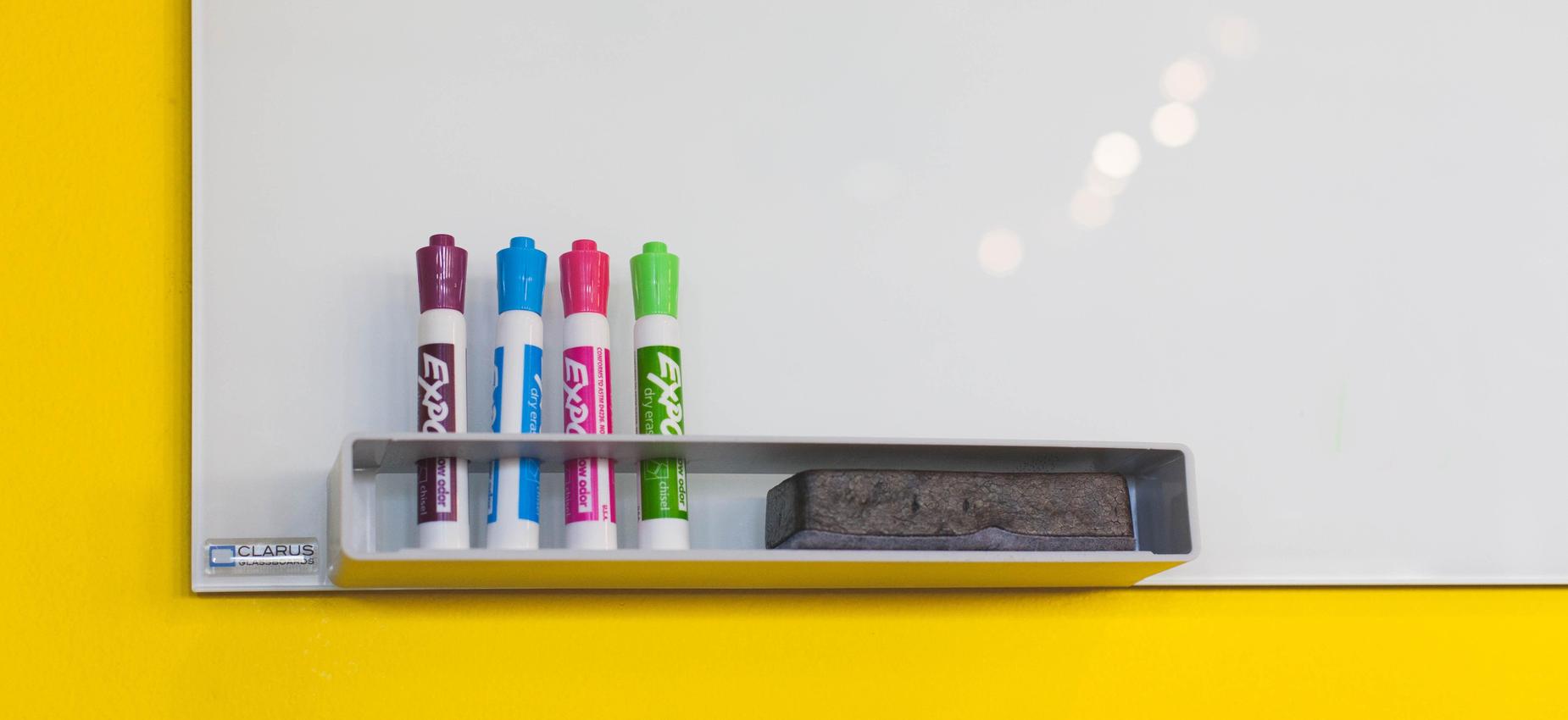 Whiteboard mounted on a yellow wall with markers and an eraser.