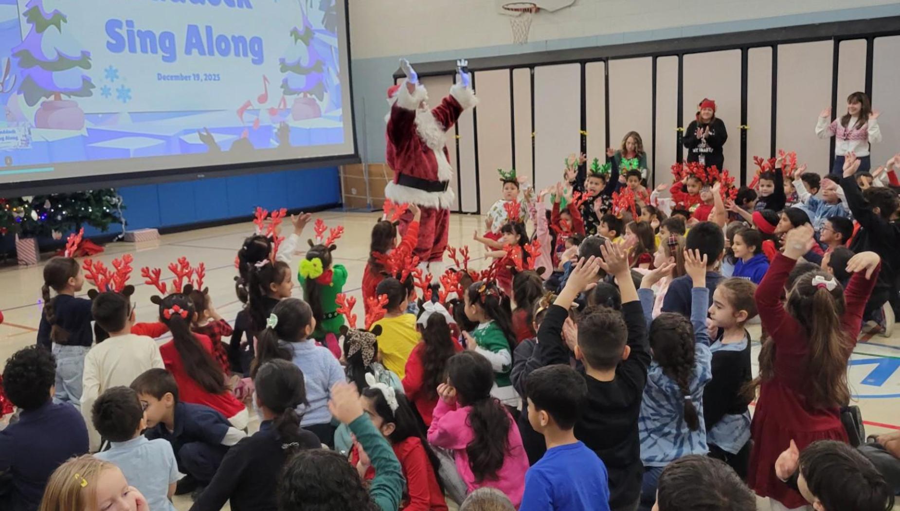 Children wearing reindeer antlers participate in a holiday sing-along event with Santa.