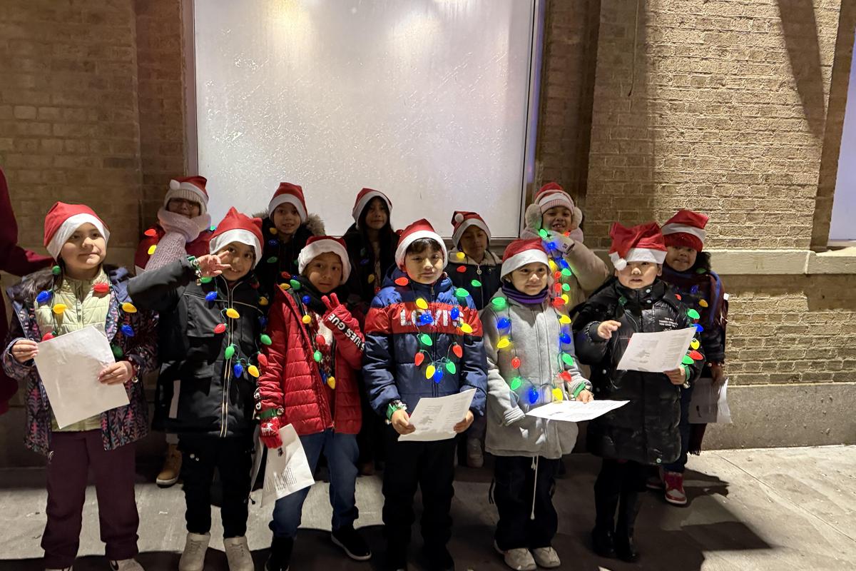 Kids wearing Santa hats and lights singing carols outside during a holiday event.