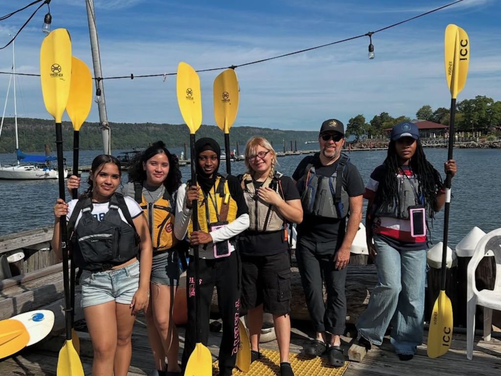 Students pose with their kayak paddles in the air