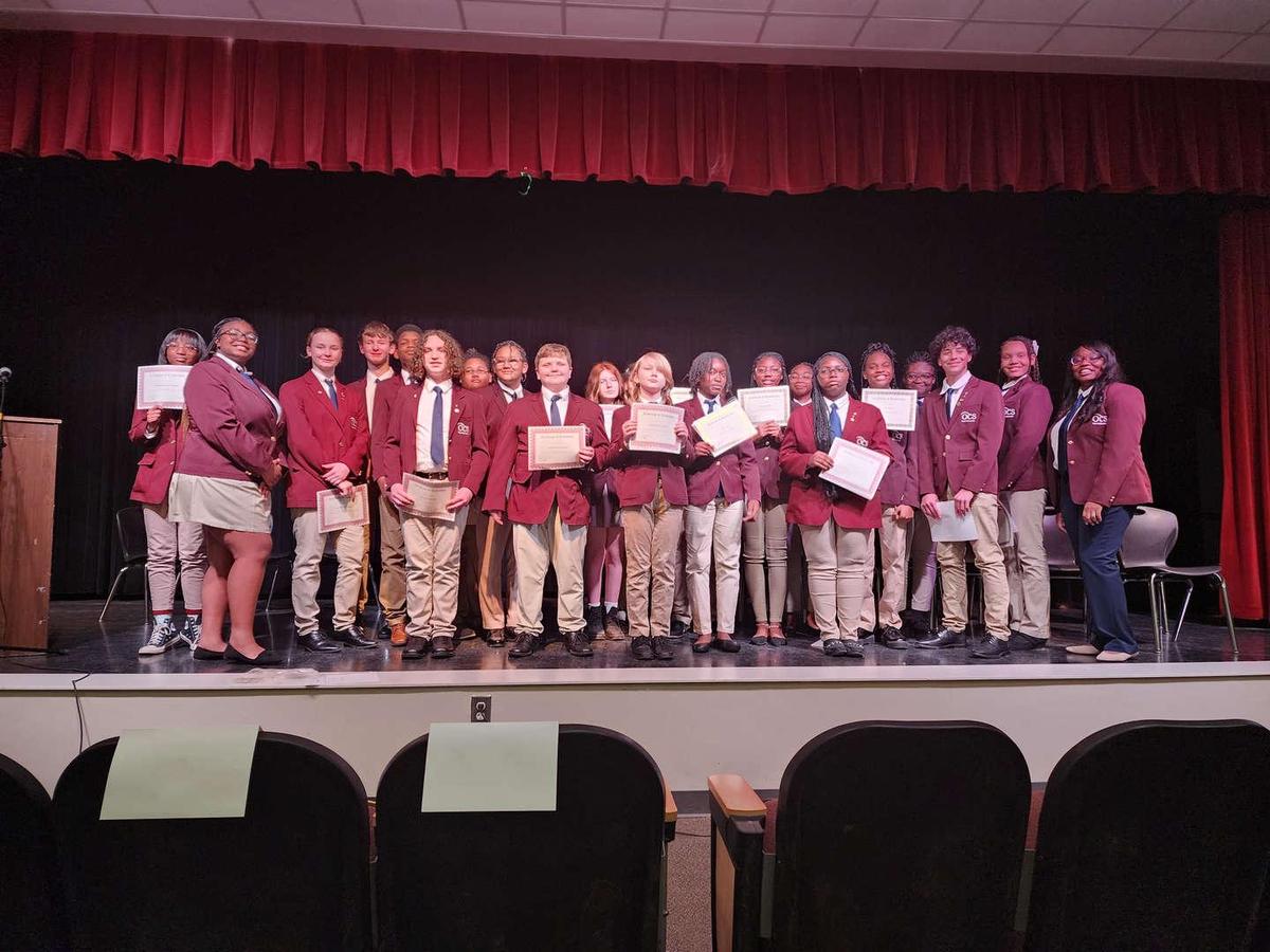 Group of students in blazers holding certificates on stage.