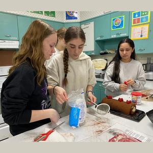 Students preparing a dessert together in a kitchen with various ingredients.