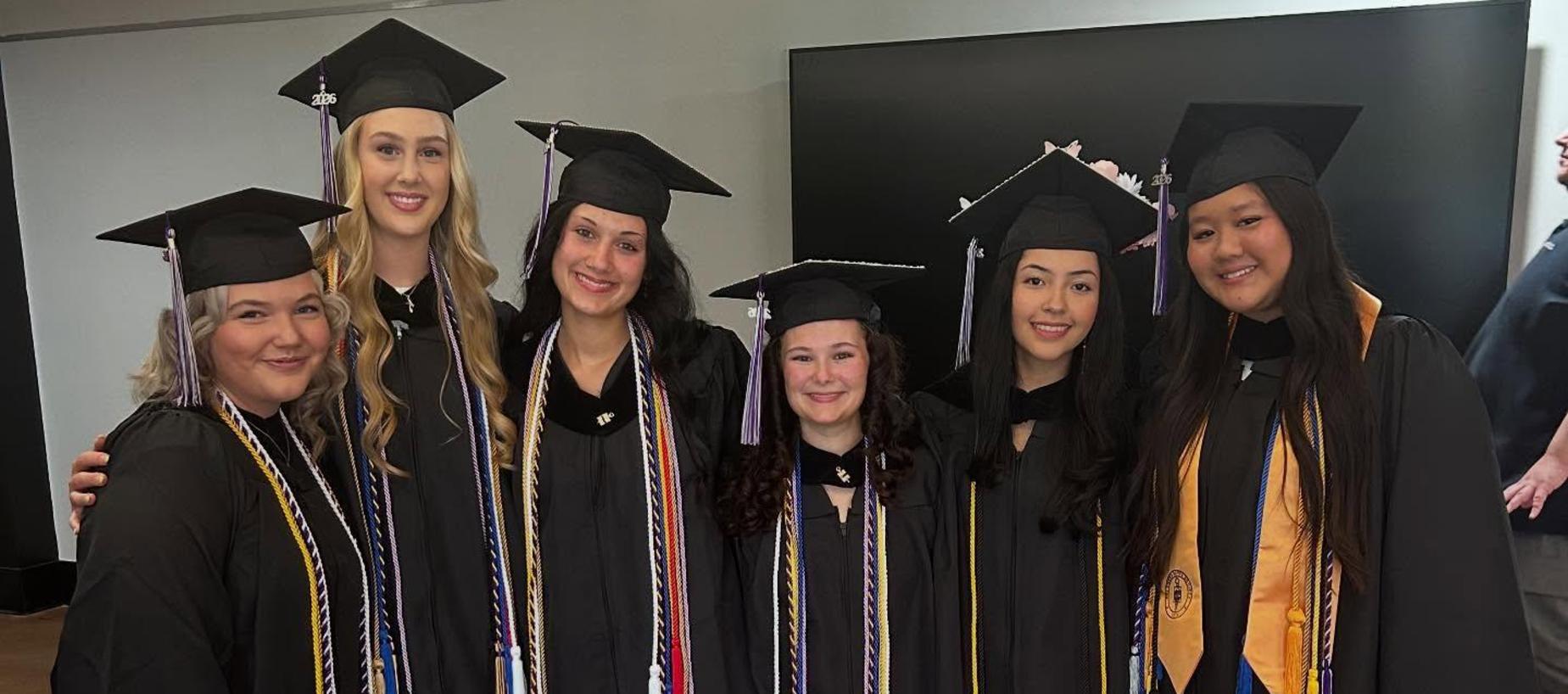 Group of seven graduates in caps and gowns, smiling together in celebration.