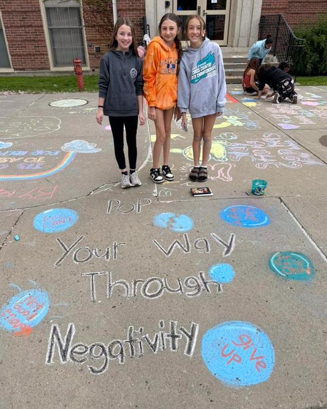 Students smile behind a sidewalk with a chalk drawing that says "Pop your way through negativity".
