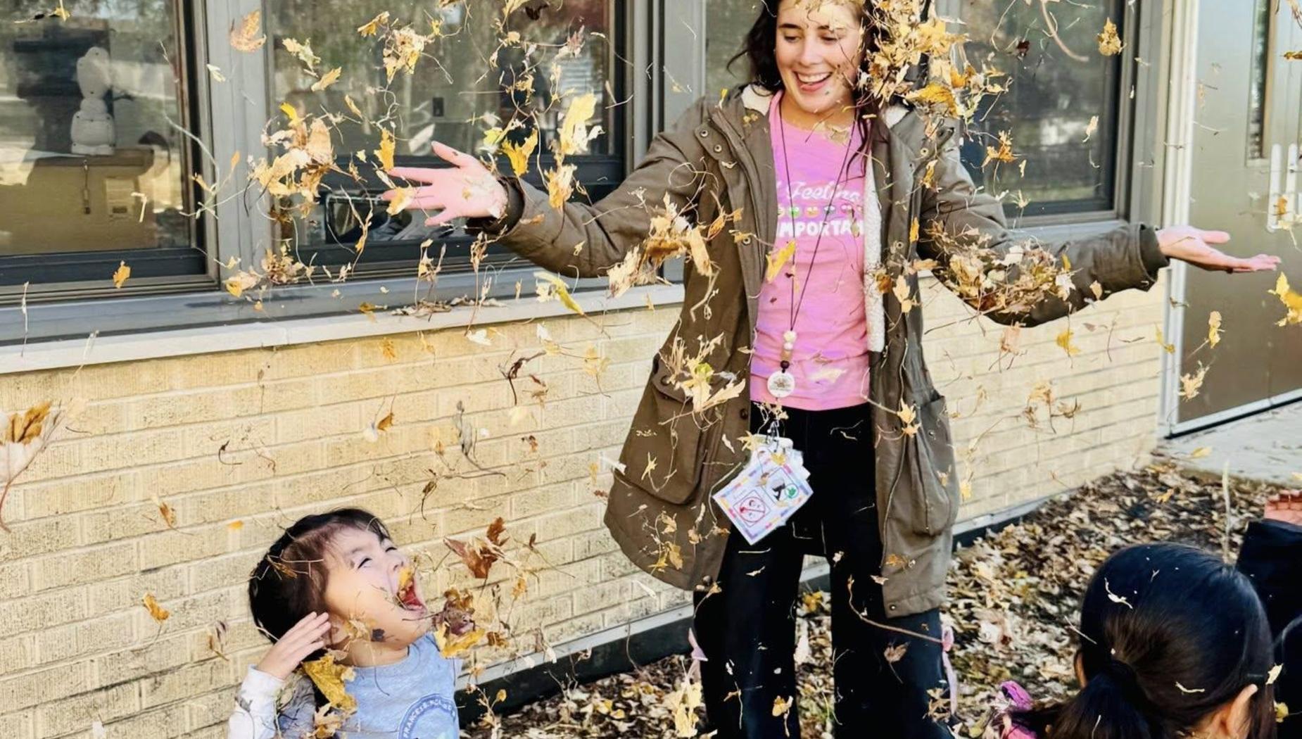 Child joyfully playing in falling leaves with an adult nearby.