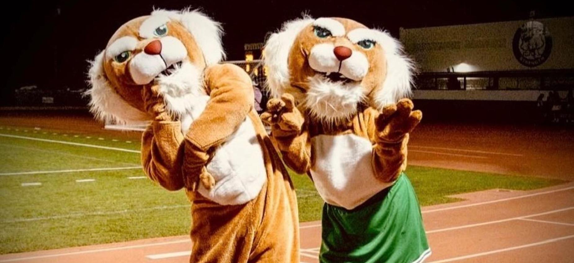 Two costumed mascots posing together on a running track.