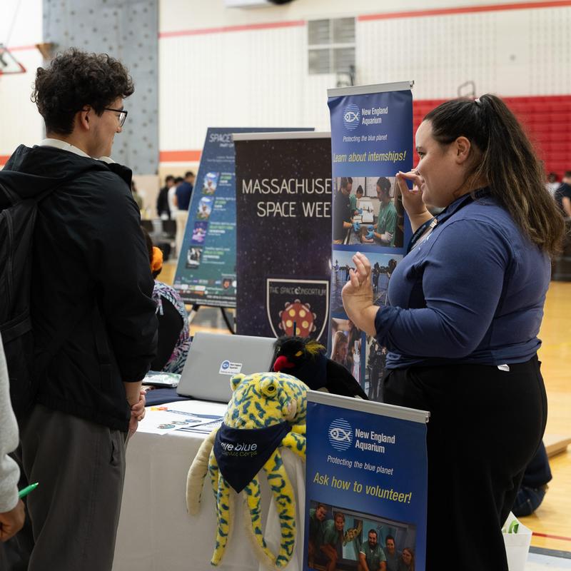 A person discussing internships at a booth with informational posters and plush sea creatures.