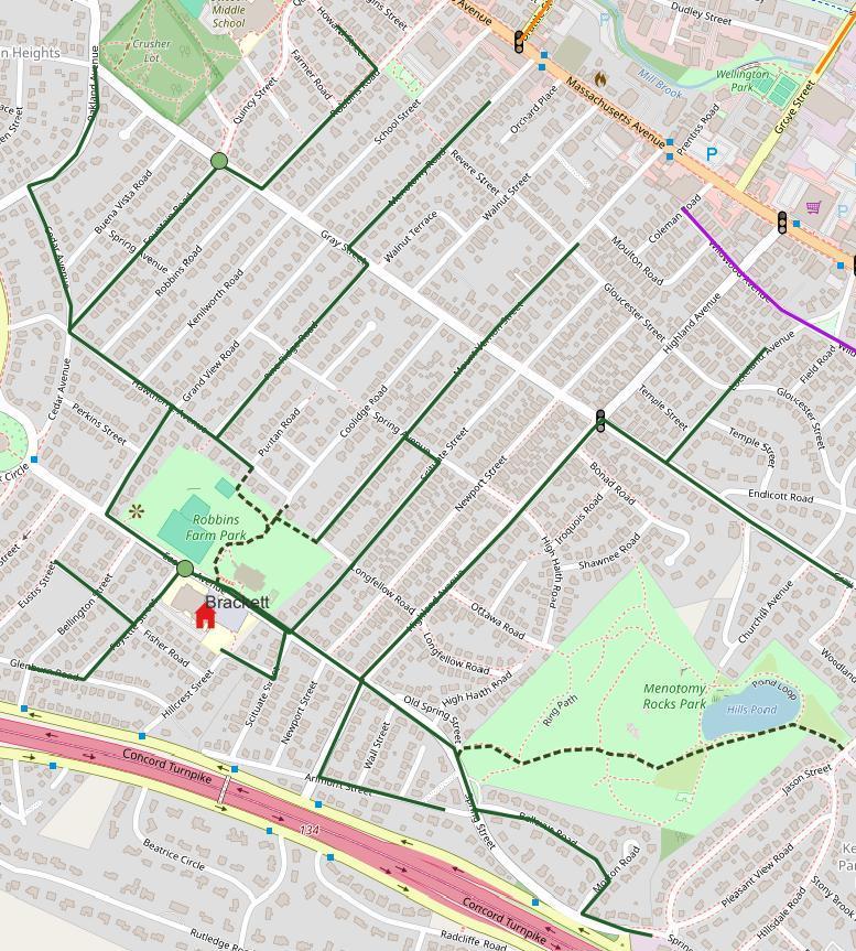 Map of the Brackett Elementary School walking route in Arlington, MA, shown in green. The route runs along several parallel streets north of the school — including Grand View Road, Gray Street, Newport Street, and Temple Street — converging near Robbins Farm Park and Brackett School on Eutis Street. A dashed segment through Menotomy Rocks Park indicates an unpaved, three-season-only path. A traffic supervisor post is marked with a green dot near the school, along with a traffic light icon further north near School Street.