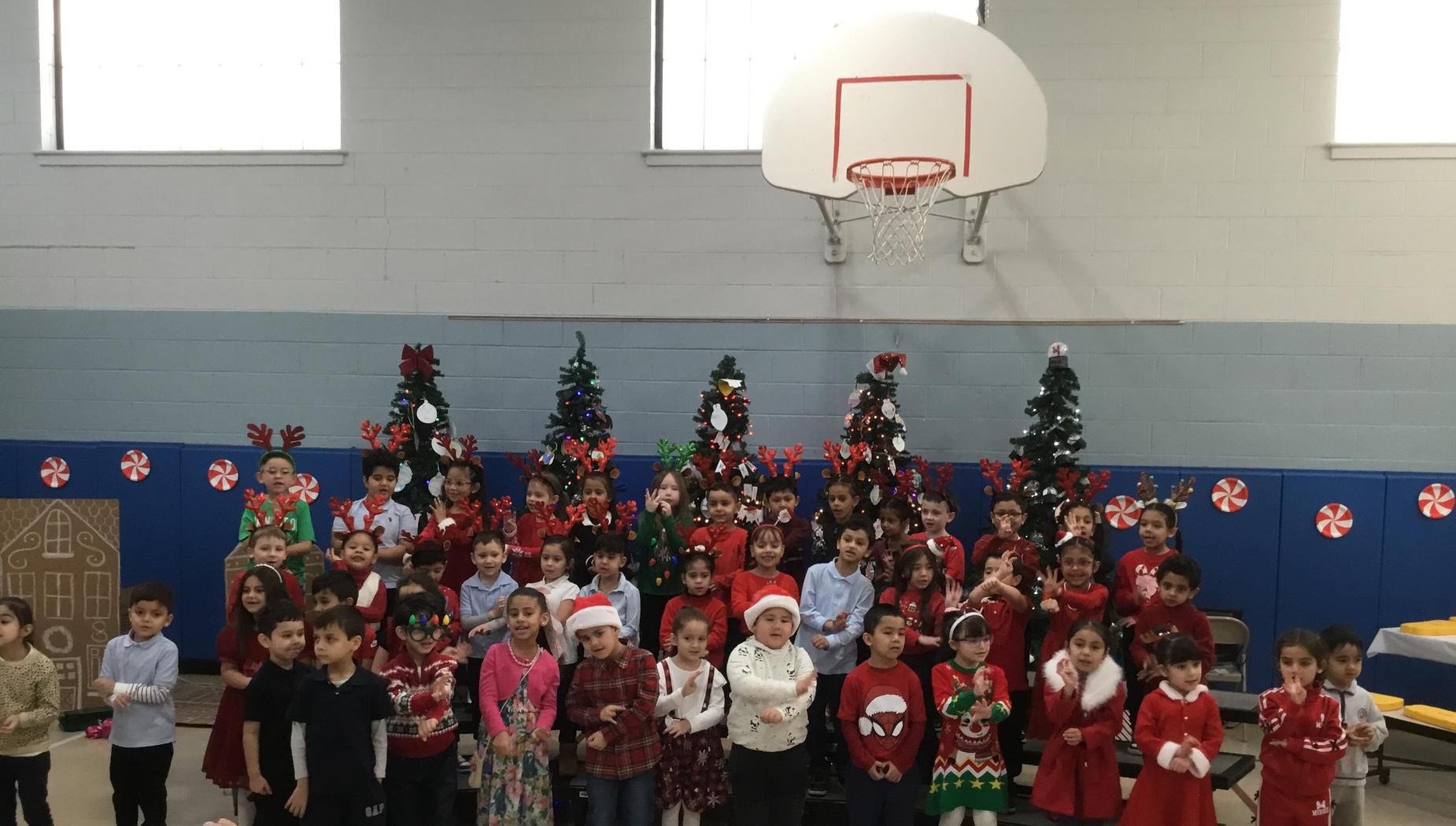 A festive group of children in holiday attire, smiling in front of decorated Christmas trees.