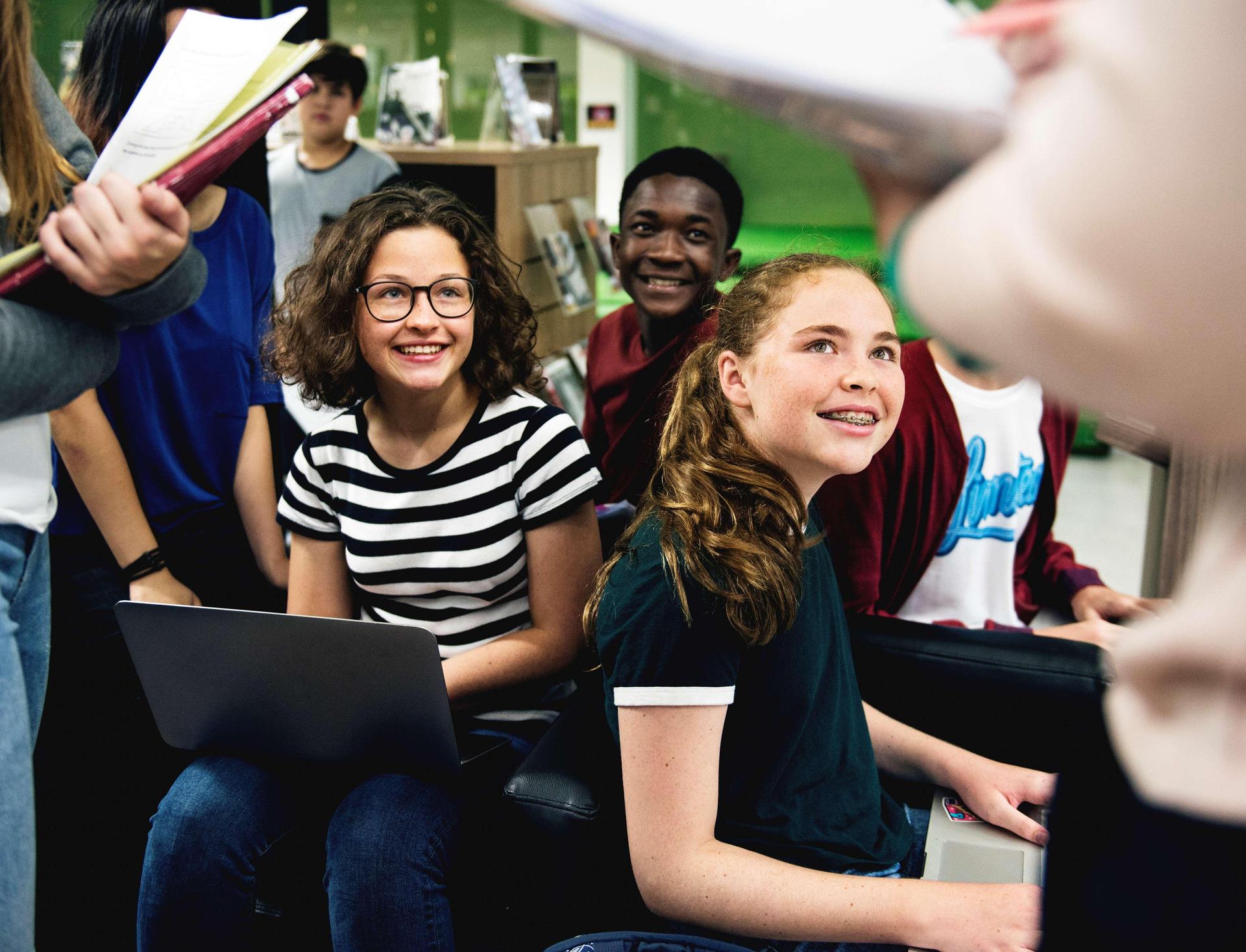 Students sitting together in a classroom, smiling and listening during a group activity.