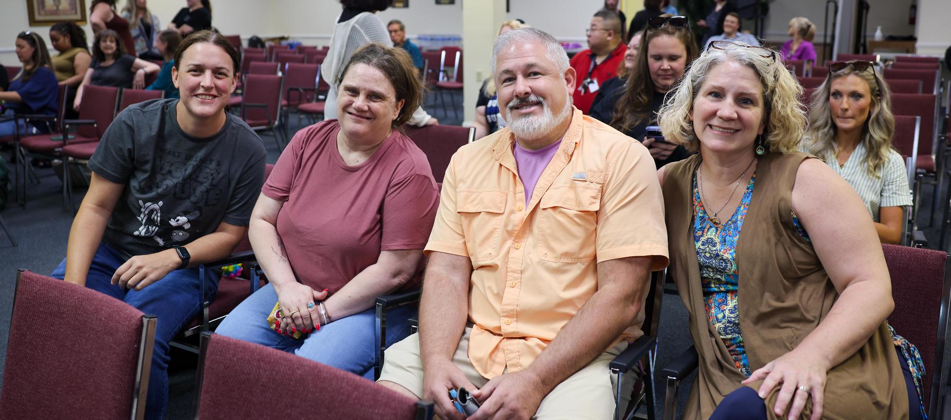 A group of four people sitting together, smiling in a gathering space.