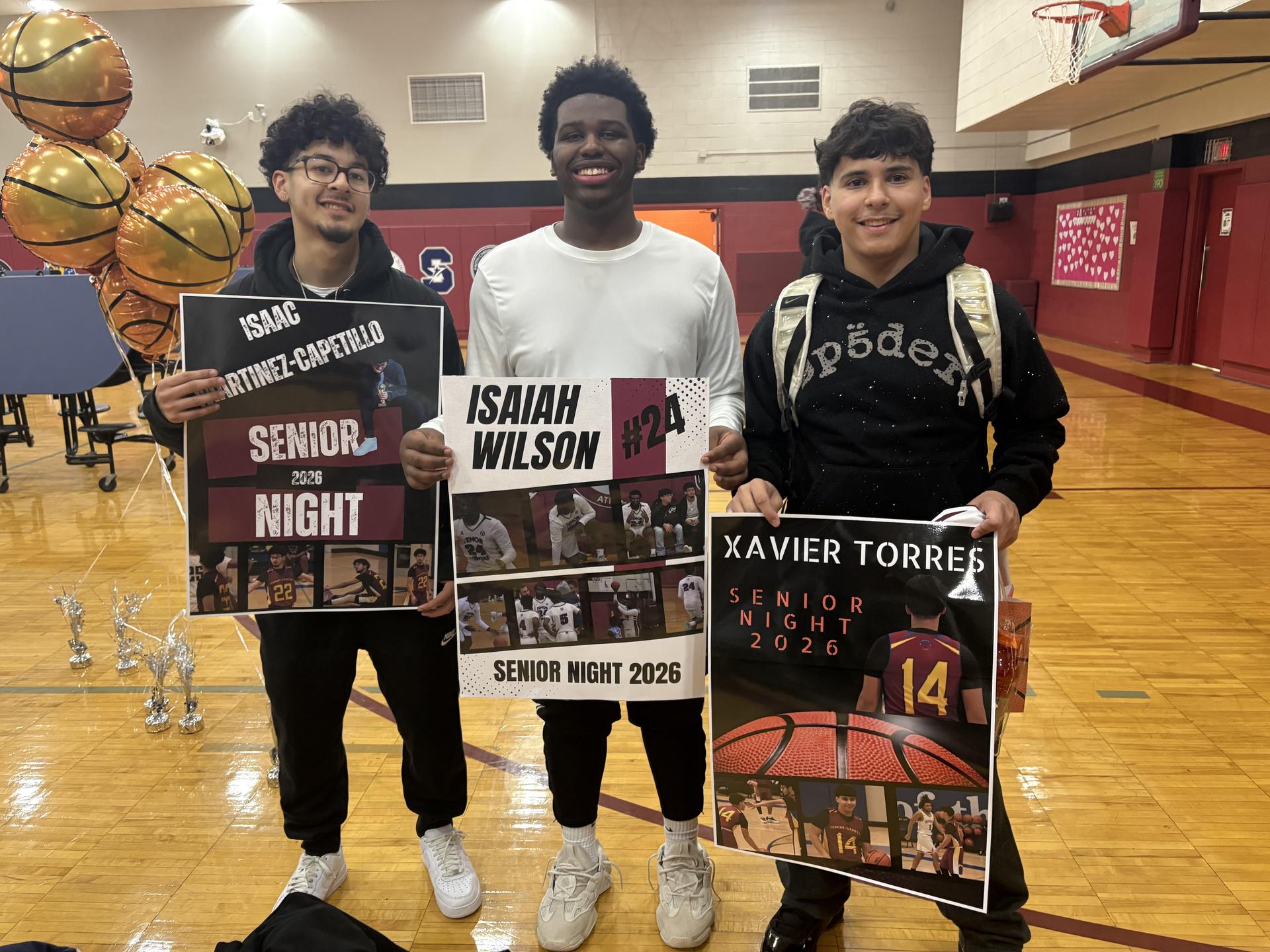 Boys basketball players smiling with posters on senior night