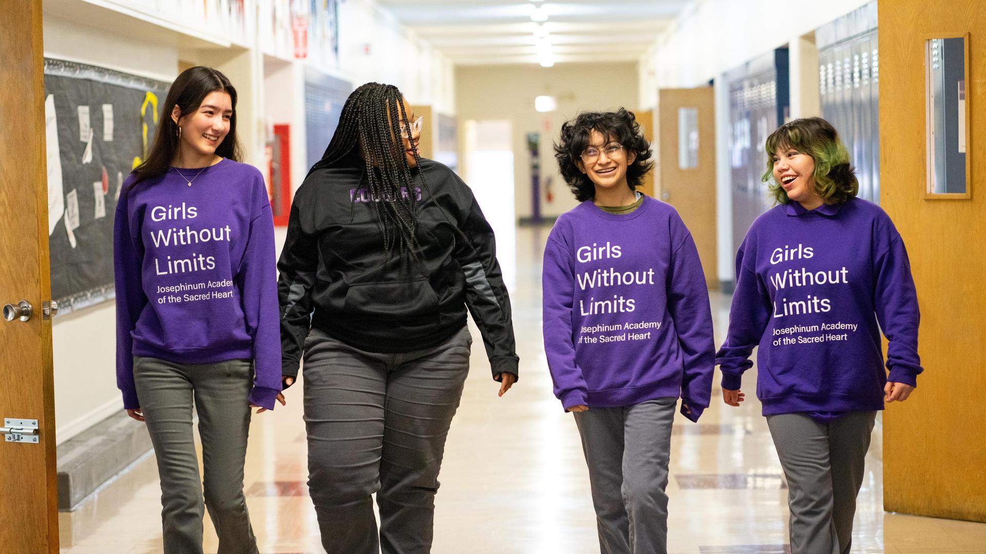 Four girls walking together in purple sweatshirts in a school hallway.