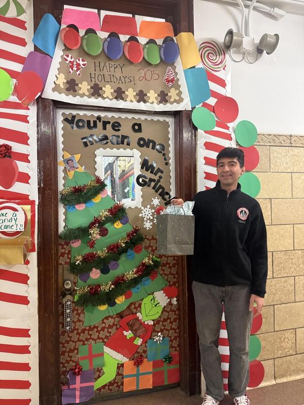 Mr. Giorgiou beside his decorated door. Door decorated with a Christmas tree, presents, and a devious looking Grinch.