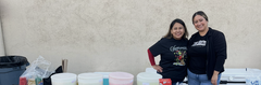 Two women behind a refreshment table for a 5th-grade fundraiser event.