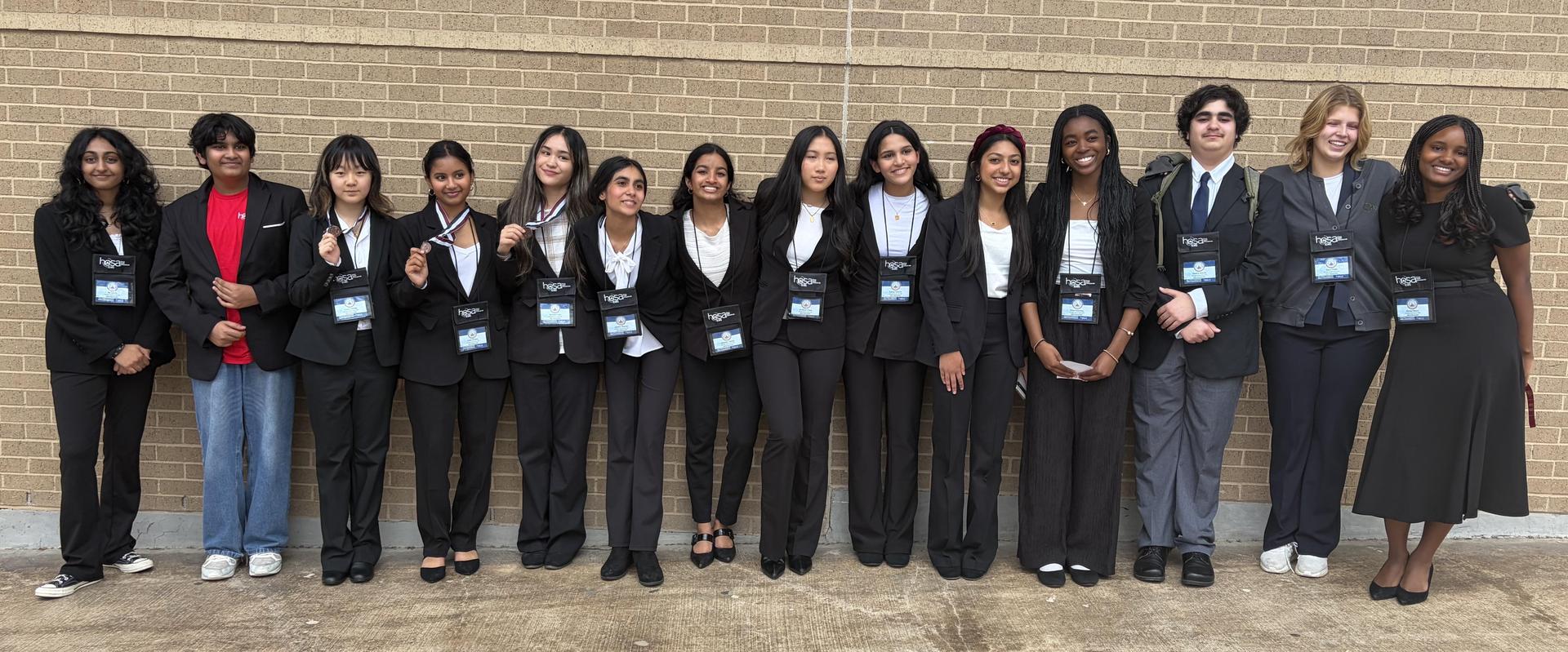 Students stand in business dress in front of a brick wall