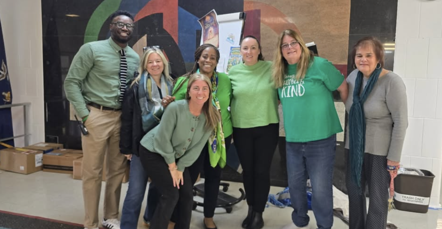 Group of people wearing green clothing, smiling together in a school setting.