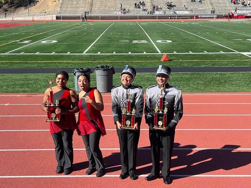 four students in parade attire show off their trophies