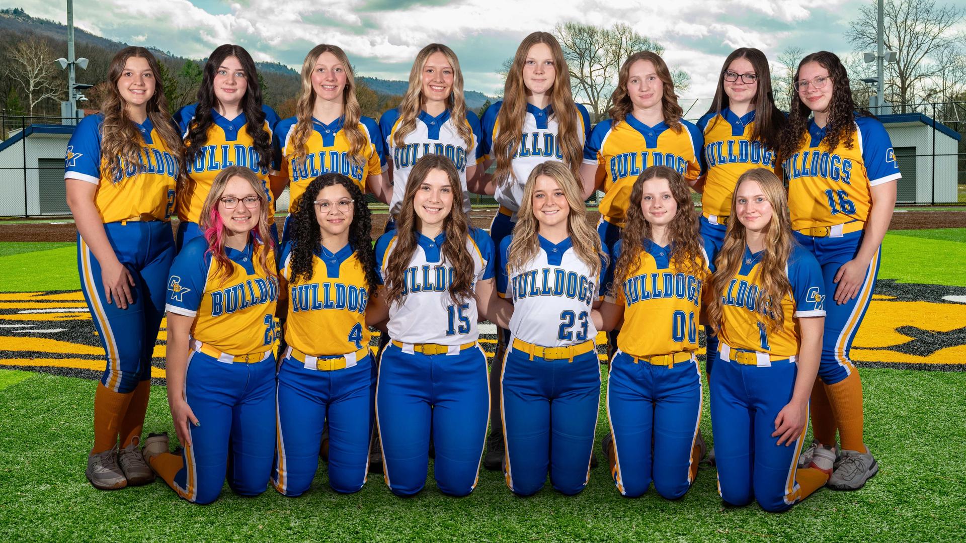 Group of high school softball players in bright uniforms posing on a field.
