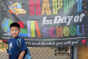 Young boy standing in front of a Happy first day of school sign