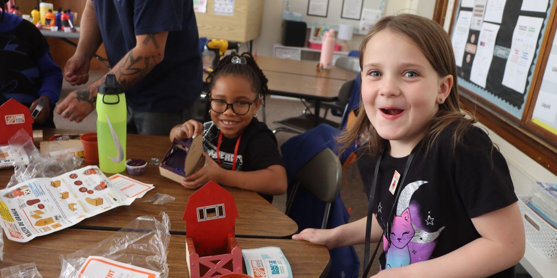 Two girls create a craft project at a table, with one laughing joyfully.
