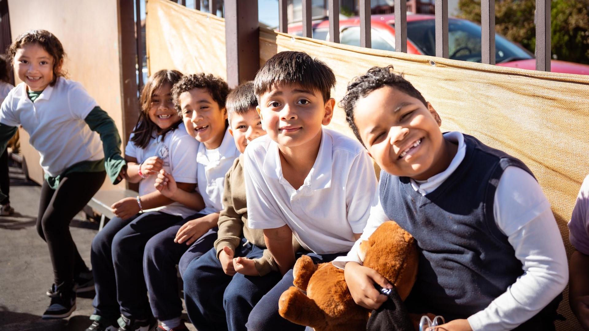 Group of smiling children sitting together, some holding toys.