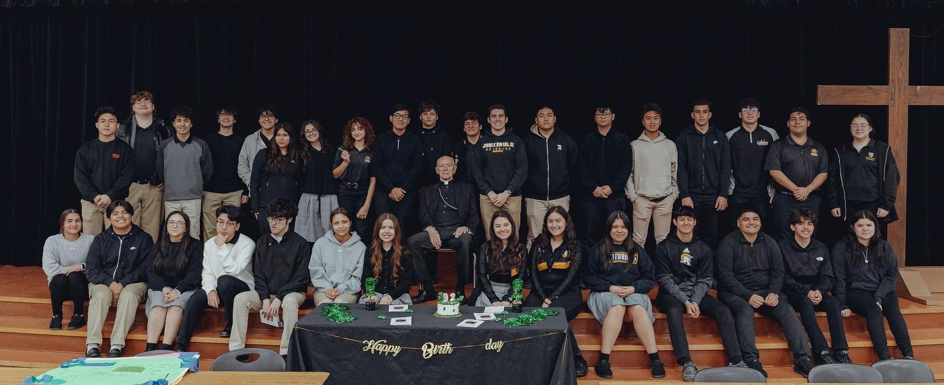 A group photo of students and adults in a school setting, celebrating a birthday.
