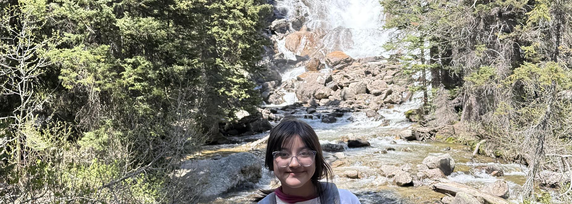 Person with glasses smiles by a waterfall and river.