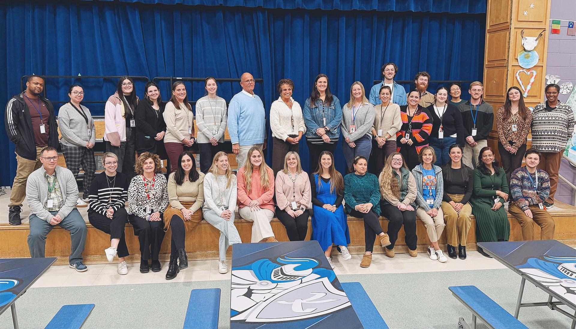 Group photo of diverse individuals gathered in a school auditorium.