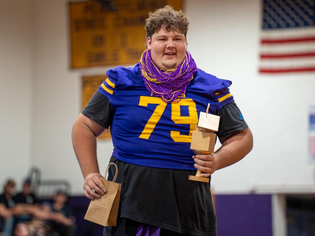 A football player wearing dozens of purple and gold Mardi Gras necklaces and holding an award.