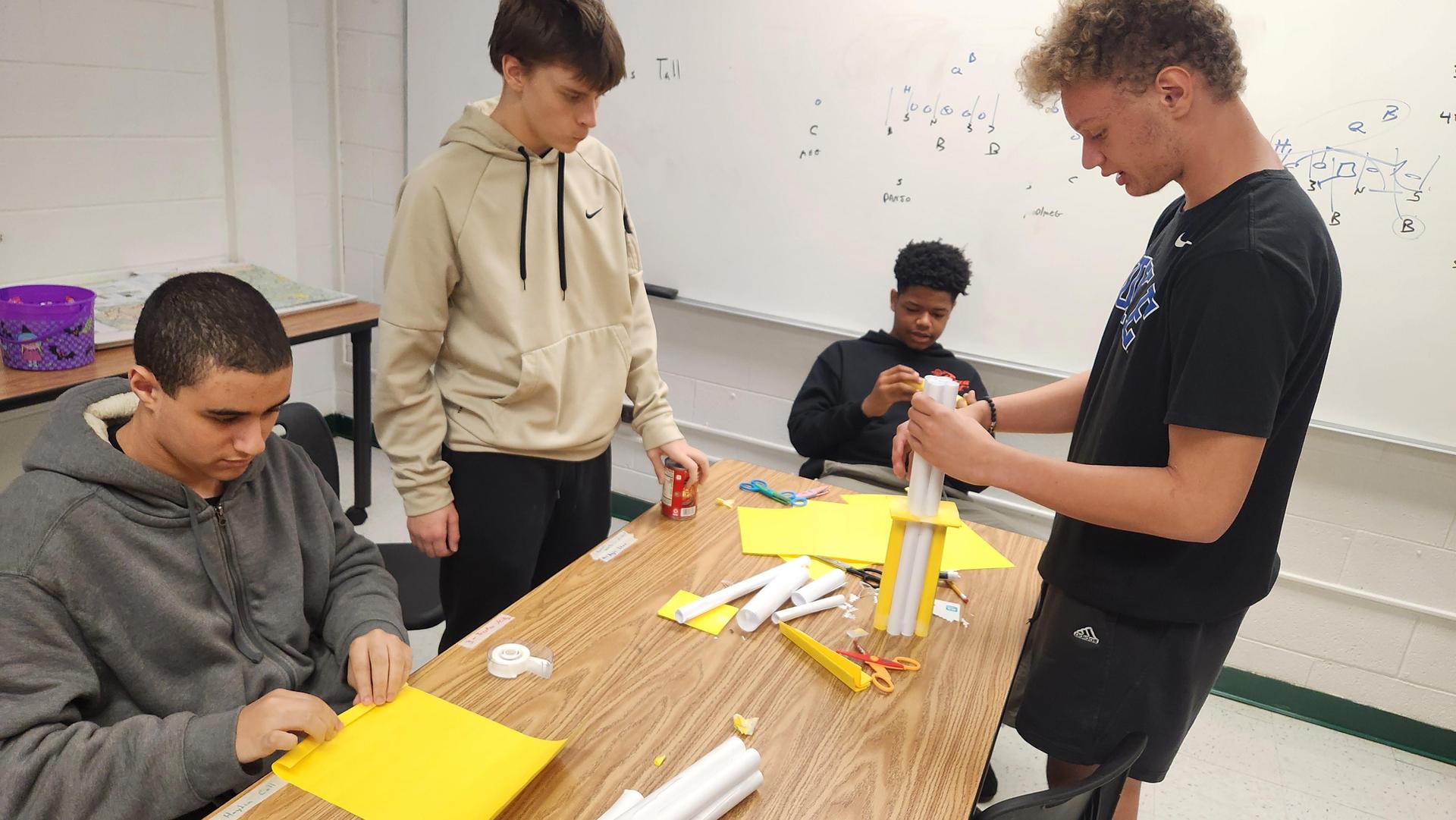 Four students working on a project with yellow materials and tower components.