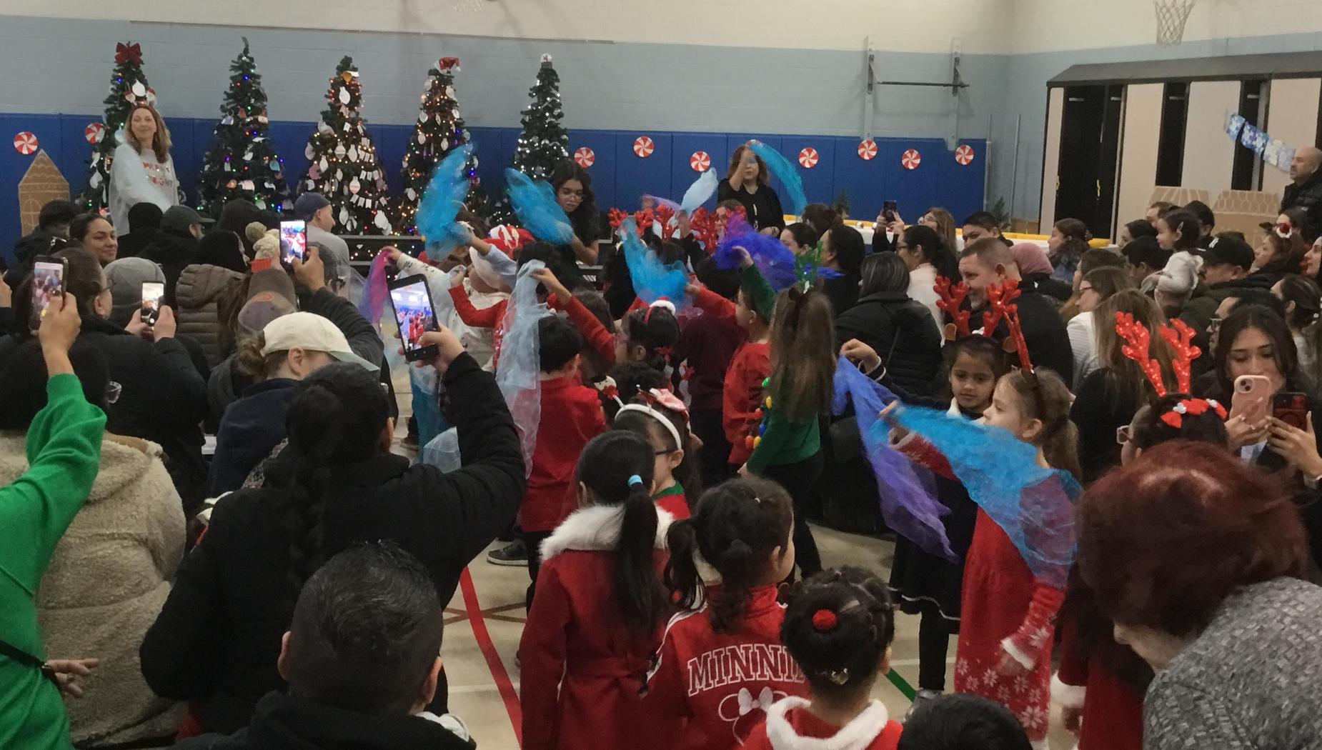 Kids dressed in festive costumes wave colorful scarves during a holiday performance.